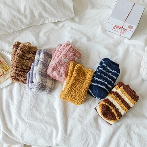 Close-up of cozy striped coral fleece socks with 3D cute ears on a white bed sheet