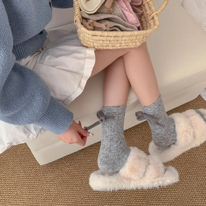Detail of grey knitted wool socks with ribbon bow and plush cross-strap house slippers