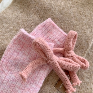 Close-up of pink wool blend socks featuring knit bow detail and craft paper tag