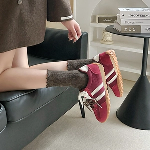 Close-up of dark red suede sneakers with white stripes and wool socks on a sofa