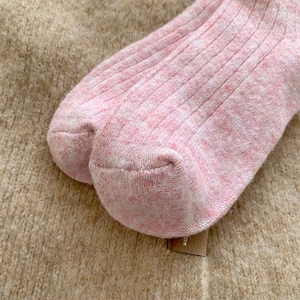 Close-up of pink wool blend socks with ribbed texture on warm plush background