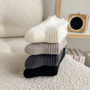 Close-up of thick ribbed knit socks in four neutral colors on a cozy wool chair