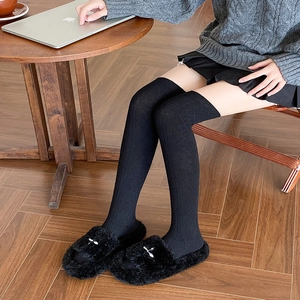 Detailed texture of black knit over-the-knee socks and fluffy slippers in home setting