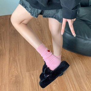 Detail of pink ribbed socks with red heart embroidery and black fuzzy cross-strap slippers