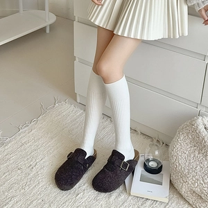 Detail view of white ribbed high socks paired with brown felt mules in a cozy room