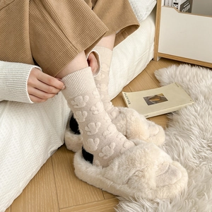 Detailed view of cream tulip jacquard wool socks worn with plush cross-strap slippers