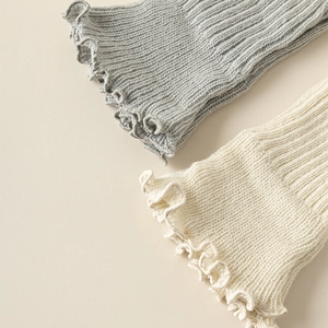Dettaglio di scaldamuscoli in maglia a coste con bordi a balze grigio e crema