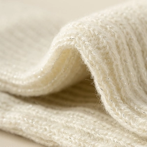 Dettaglio ravvicinato di scaldamuscoli in maglia bianco crema con sottili fili glitter