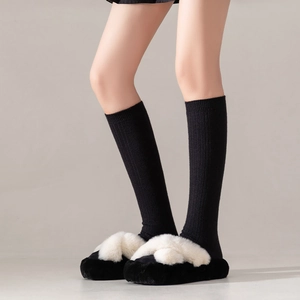 Detail of warm black knitted socks paired with black and white faux fur crossover slippers