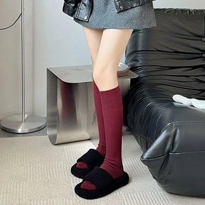 Close-up of ribbed knit dark red socks paired with black plush slippers on a home sofa