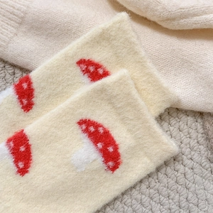 Close-up of soft fuzzy cream knit socks featuring cute red and white mushroom patterns