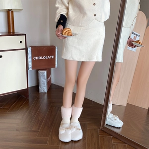 Close-up of white plush leg warmers and cozy faux fur home slippers with a bow