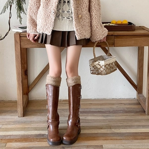 Close-up of brown long boots featuring faux fur trim and decorative metal buckles