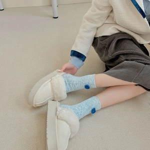 Détail de chaussons en peluche crème à semelle compensée et chaussettes à fleurs bleues