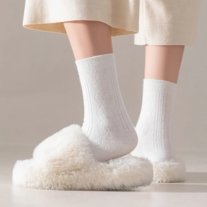 Close-up of white argyle textured knee-high socks paired with cozy plush slippers
