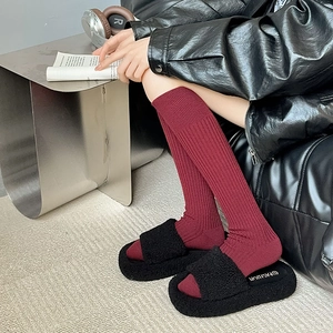 Detail of burgundy ribbed socks paired with black plush platform slippers on a sofa
