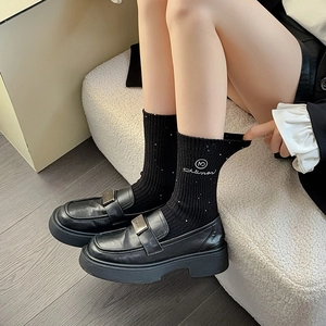 Close-up of black platform loafers with metal buckles and ribbed mid-calf socks style
