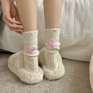 Detail of knitted cashmere socks with pink woven label and plush beige slippers