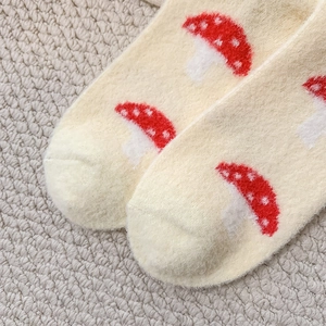 Detailed macro view of soft white plush socks featuring cute red mushroom patterns