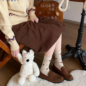 Detail of wool socks with bow and bear patterns paired with brown loafers and corduroy skirt