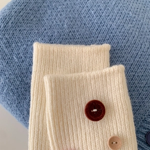 Close-up of white ribbed knit fabric featuring decorative vintage buttons on blue background