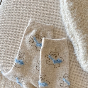 Detail of soft beige knit wool socks featuring a blue fuzzy cartoon cat patch
