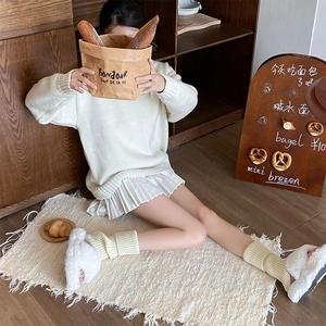 Close-up of cream knit leg warmers paired with a white pleated skirt and plush slippers
