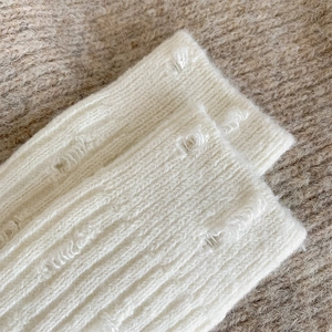 Close-up of white knitted wool socks featuring unique distressed ripped hole details