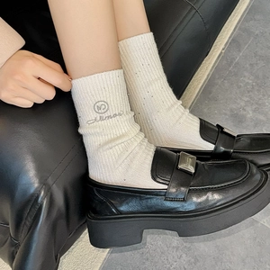 Close-up of white ribbed wool socks with rhinestone detail and black platform loafers