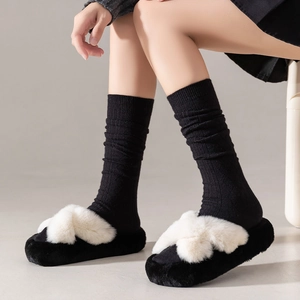 Close-up of white plush crossover slippers with black ribbed socks for home comfort