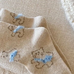 Detail of warm beige knit socks featuring cute bear pattern and 3D blue plush bow decoration