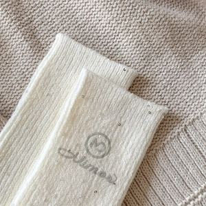 Close-up of white wool socks featuring shiny silver sequins and glitter atmos logo detail
