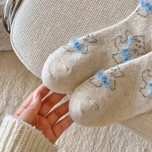 Detailed macro view of soft beige wool knit socks featuring a cute 3D blue pom-pom bear