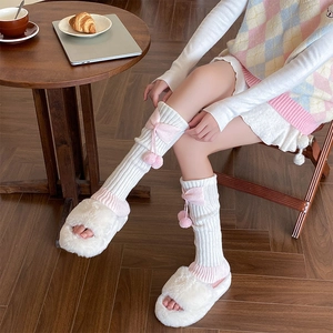 Détail de jambières en tricot avec nœuds roses, pompons et pantoufles en peluche
