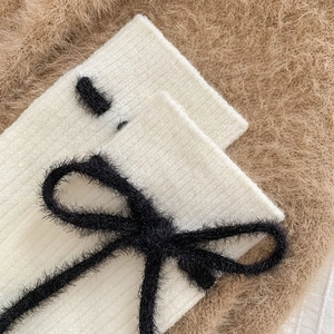 Detailaufnahme der weißen Strickstulpen mit flauschiger schwarzer Schleifenverzierung
