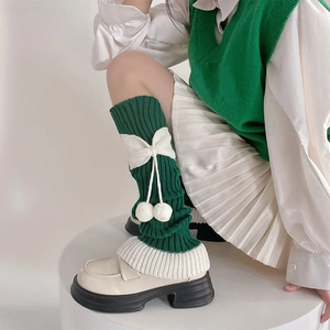 Détail de jambières en tricot vert avec nœuds blancs et pompons en peluche sur les côtes