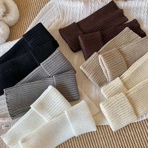 Flat lay of ribbed knit leg warmers in six colors on a warm white knitted background