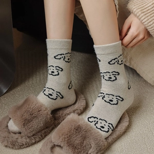 Dettaglio di spesse calze di lana beige con motivi di cani e pantofole di peluche marroni