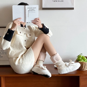 Detail of cream cable knit leg warmers paired with plush bow slippers for winter