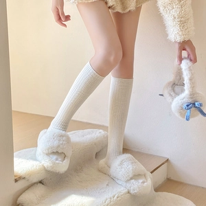 Detail of cream plush slippers and ribbed thermal socks on a cozy rug in home setting