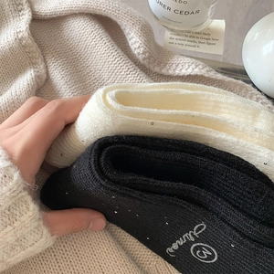 Detail of wool socks with silver sequins and embroidered M logo in warm home setting