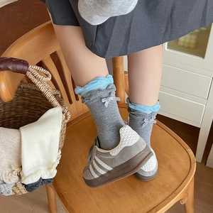 Detail of grey knitted crew socks with light blue ruffles and a small silver bow tie