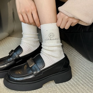 Close-up of white ribbed wool socks with silver logo embroidery and black loafers