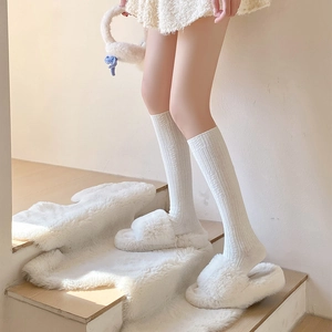 Detail of white ribbed knit calf socks paired with plush slippers on wooden steps