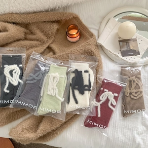Nahaufnahme von Wollsocken mit Plüschschleife in verschiedenen Farben auf Bettwäsche