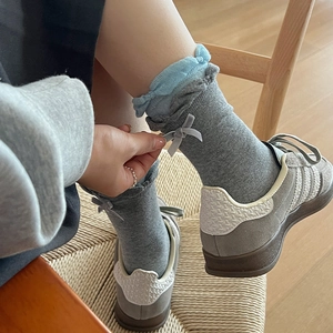 Grey frilly crew socks with blue lace trim and bow accent shown with suede sneakers