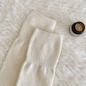 Détail de chaussettes hautes en tricot blanc crème sur tapis en fausse fourrure blanche
