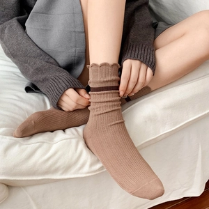 Brown ribbed crew socks with ruffle cuffs and stripes worn on a sofa in a cozy home setting