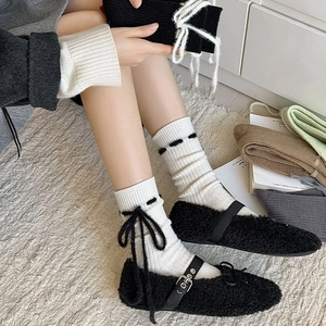 Japanische schwarze Plüsch-Mary-Janes mit weißen Schleifen-Socken auf strukturiertem Teppich