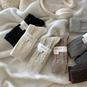 Close-up of thick cable knit wool socks in neutral colors on a soft white background